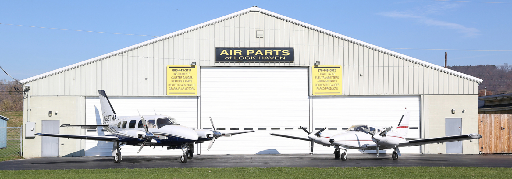 Two small planes parked outside of an Air Parts of Lock Haven hangar
